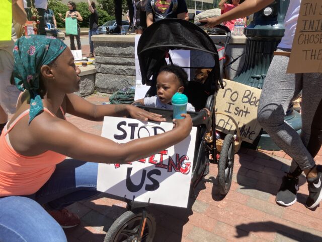 Early afternoon at the center of the protest at Vance Memorial was a small black boy in his stroller. His mother taped a sign saying, “Stop Killing Us.” Top right: Protestor hoisting an amplified speaker for vocal leaders to speak as they marched out of Downtown Asheville. 